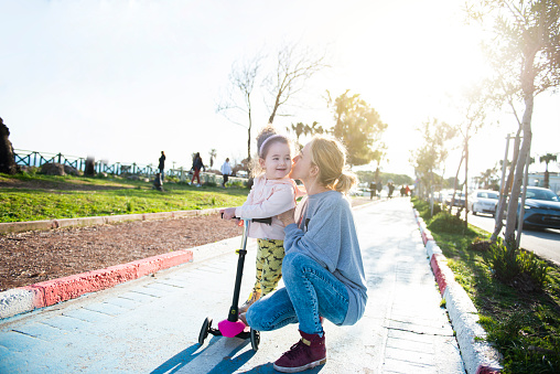 Baby girl spending happy time with her mother.  Girl playing with her mother and riding a scooter in the park in spring weather