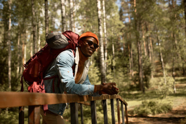 喜びに満ちた黒人の若者は森の中で旅行を過ごし、キャンプのための未知の道を探します。新しい場所、楽しい余暇、野生動物を探索してください。旅行と新しい地平線、放浪者、山の概念� - footpath wood horizon nature ストックフォトと画像