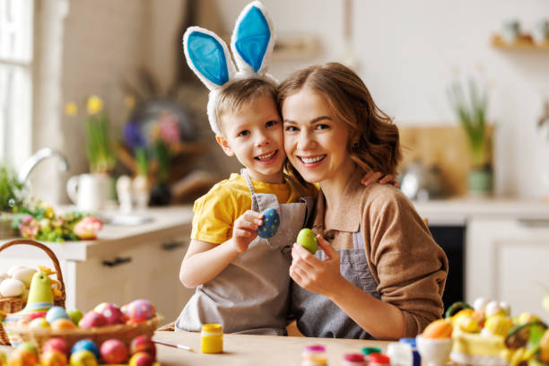 istock Loving young mother teaching happy little kid son to decorate Easter eggs while sitting in kitchen 1382379339