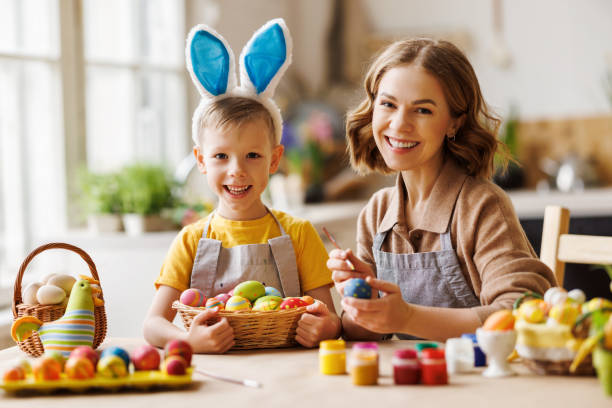 istock Loving young mother teaching happy little kid son to decorate Easter eggs while sitting in kitchen 1382381181
