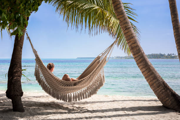 vacanze al mare con donna che si rilassa sull'amaca tra palme da cocco, sabbia bianca, cielo blu e acqua turchese. resort panoramico dell'isola alle maldive, destinazione di viaggio perfetta. - hammock beach vacations tropical climate foto e immagini stock