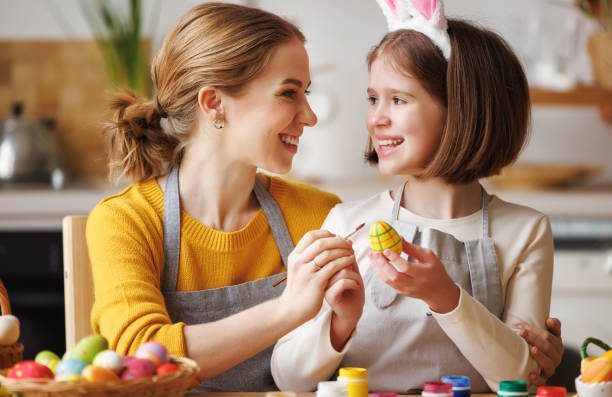 istock Loving young mother teaching happy   kid daughter to decorate Easter eggs while sitting in kitchen 1382384437