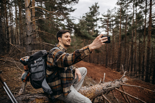 Young smiling caucasian man using a smart phone in the nature. Using technology in the nature concept.