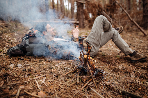 Male mountaineer makes a campfire in the middle of the forest to warm up a bit