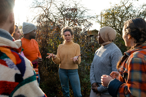 A multiracial group of volunteers wearing warm casual clothing and accessories on a sunny cold winters day. They are talking before they start working on a community farm, planting trees and performing other tasks.