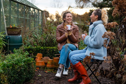 Volunteers sitting outdoors wearing warm casual clothing on a sunny cold winters day. They are resting and having a tea break from working on a community farm, looking after crops and performing other sustainable and environmentally friendly tasks. They are laughing and talking together, drinking hot drinks.