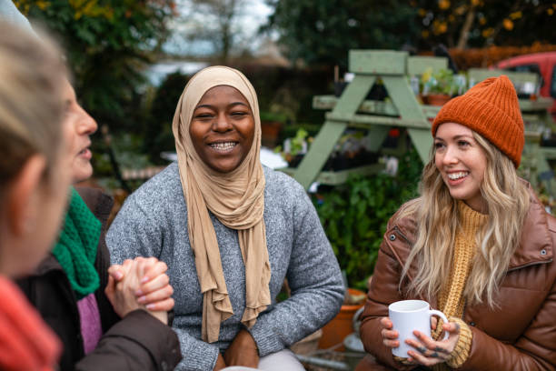 Diverse Women Volunteers Volunteers sitting outdoors wearing warm casual clothing on a sunny cold winters day. They are resting and having a tea break from working on a community farm, looking after crops and performing other sustainable and environmentally friendly tasks. They are laughing and talking together, drinking hot drinks. northumberland stock pictures, royalty-free photos & images