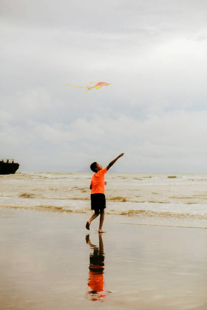 In holiday, Little boy standing on the beach holding a kite string, enjoying a calm seaside moment during a sunny family vacation