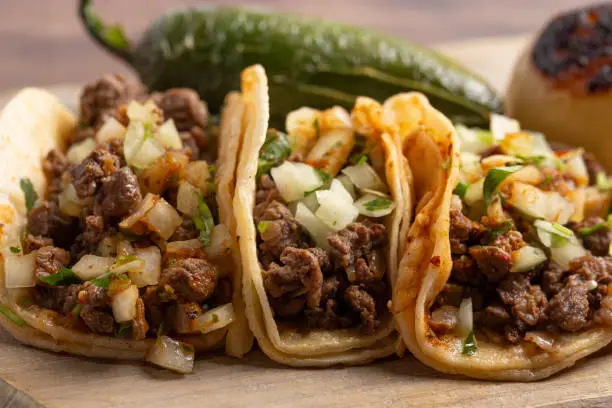 Three Steak Street Tacos in a Row on a Wooden Platter