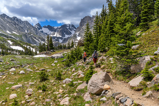 Ward, Colorado, USA - July 2, 2021: Two well-equipped mountaineers hiking on Pawnee Pass Trail towards rugged Indian Peaks on a sunny Summer day at Indian Peaks Wilderness.