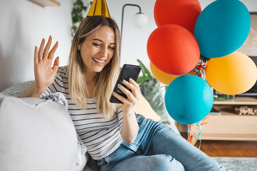 A young woman in the living room celebrating her birthday at home and talking with friends on video call.