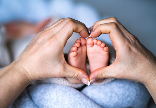 Newborn baby's feet on mother heart shaped hands at home