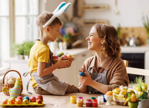 istock Loving young mother teaching happy little kid son to decorate Easter eggs while sitting in kitchen 1382417269