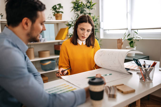 Professionals discussing blueprints on desk in small office
