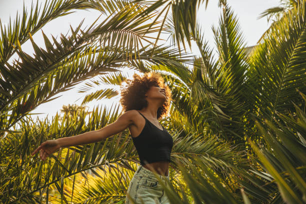 jolie jeune femme afro au milieu des palmiers - fashion photos et images de collection