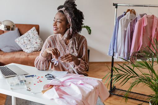 A young African American seamstress works in her apartment. She is smiling while working