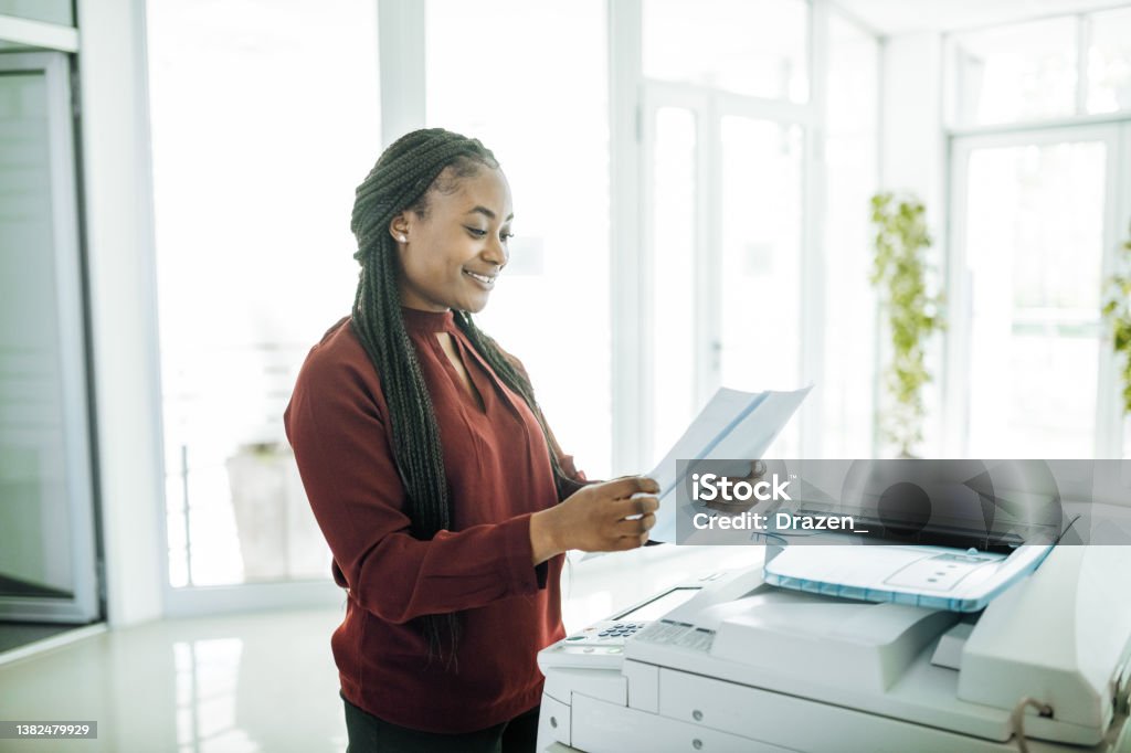 African-American businesswoman working in office after reopening, using photo copier Employees and coworkers are back in the office after lockdown, working together and wearing face masks Computer Printer Stock Photo