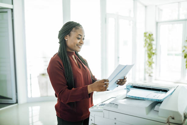 African-American businesswoman working in office after reopening, using photo copier Employees and coworkers are back in the office after lockdown, working together and wearing face masks reopening photos stock pictures, royalty-free photos & images