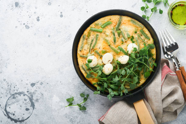 Omelet with spinach, green beans, potato and spinach healthy food in black frying pan on grey stone old rustic background. Traditional frittata for breakfast Eggs tortilla Top view flat lay Copy space stock photo