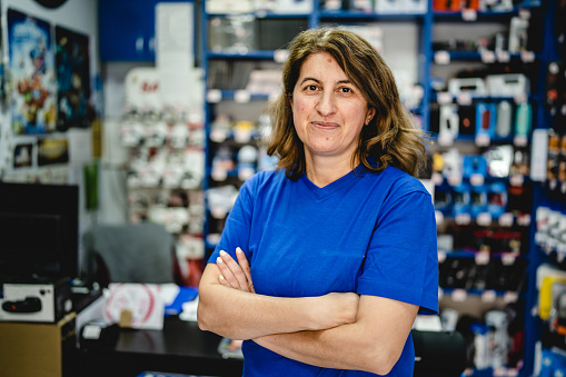 Front view portrait of mature adult caucasian one woman standing in the electronics store small business owner female entrepreneur serious looking to the camera wearing blue t shirt real people