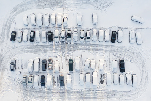 A parking lot in winter with many cars covered in snow.
