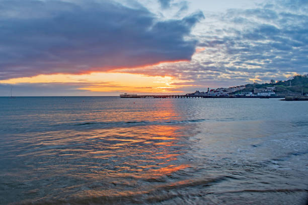 An orange sunrise splits the reflected split sea at Swanage