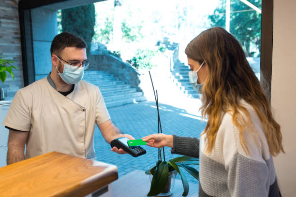 istock Receptionist holding credit card reader device receiving contactless payment from patient 1382482453
