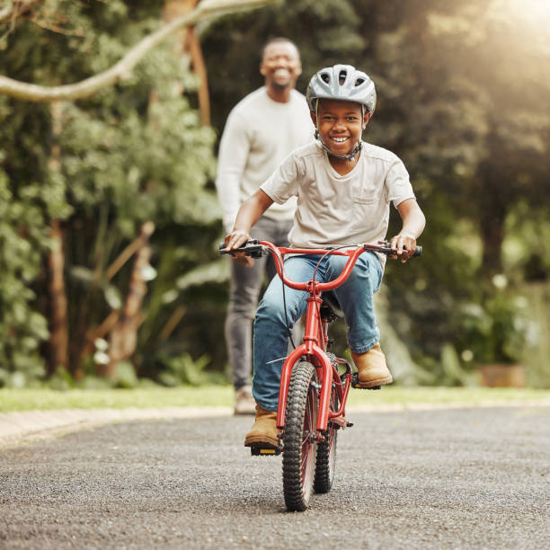 aufnahme eines entzückenden jungen, der mit seinem vater im freien fahrrad fahren lernt - radfahren stock-fotos und bilder