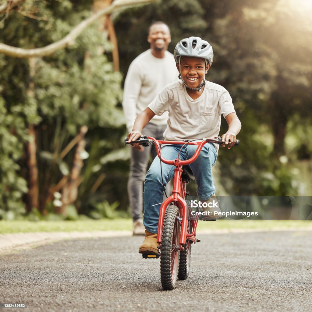 Shot of an adorable boy learning to ride a bicycle with his father outdoors Young boy learning to ride a bicycle Cycling Stock Photo