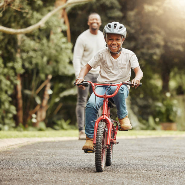 shot of an adorable boy learning to ride a bicycle with his father outdoors - cycling imagens e fotografias de stock