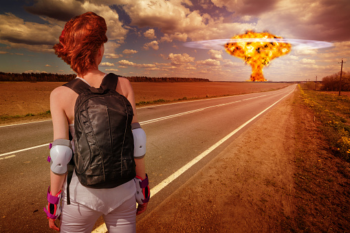 Active young woman in sportswear looking at distant nuclear explosion in the field. Fantastic apocalyptic landscape