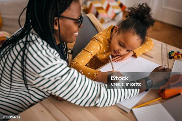 Mother Assisting Daughter In Writing Homework At Home Stock Photo - Download Image Now