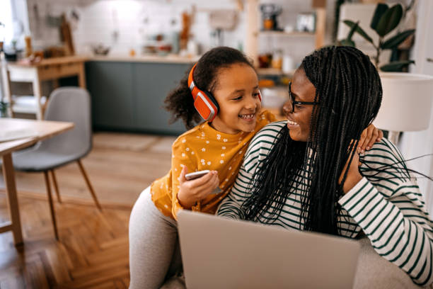 girl listening music standing by mother working on laptop at home - parent mother music listening imagens e fotografias de stock