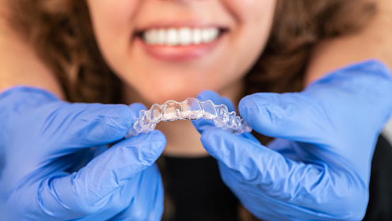 Orthodontist doctor in gloves putting silicone invisible transparent braces on woman's teeth in dentist clinic, mouth closeup view. Correcting teeth treatment and cure in dentistry.