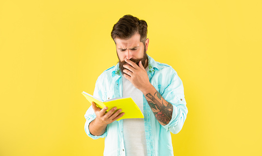 serious hipster guy reading notebook on yellow background, curiosity.