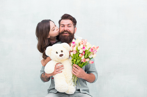 Father I love you. Happy daughter kiss father. Bearded man and little child hold flowers and toy. Happy family celebrate holiday. Love and care. Birthday anniversary. Fathers day. Congratulations.
