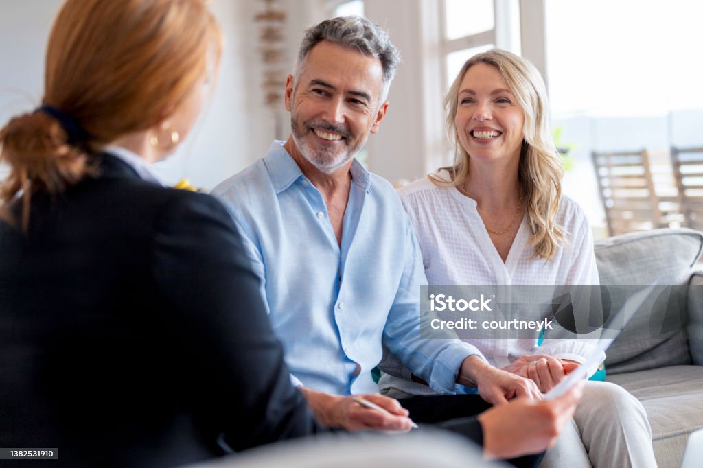 Happy mature couple meeting investments and financial advisor at home. Happy mature couple meeting investments and financial advisor at home. They are happy and smiling sitting in the living room. Customer Stock Photo