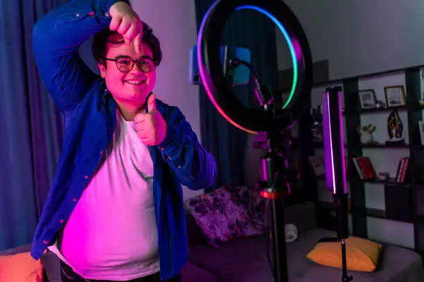 Photo of overweight young man filming videos at home and talking to camera set on ring light