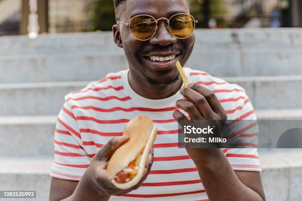 Portrait Of A Young Africanamerican Man Is Eating Hot Dog And Smiling Stock Photo - Download Image Now