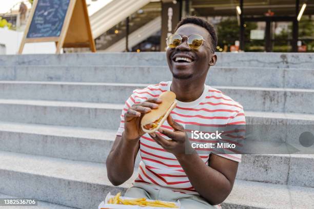 Young Africanamerican Man Is Eating Hot Dog And Smiling Stock Photo - Download Image Now