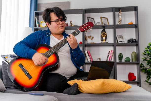 overweight boy learning online how to play guitar overweight boy learning online how to play guitar chubby arab stock pictures, royalty-free photos & images