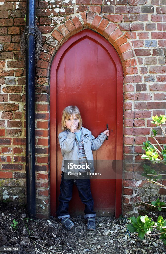 child secret door Child by small secret door with finger to lips to sign hush. kid by red wood entrance Anticipation Stock Photo