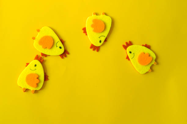 Four yellow felt decorative chickens arranged in a semicircle on a yellow background. Minimal concept, cute Easter card with a copy of the place for the text.