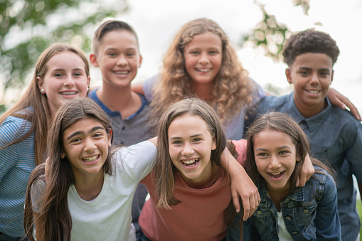 A large group of Elementary students huddle together closely outside as they pose for a portrait.  They are each dressed casually and are smiling as they enjoy time outside together.