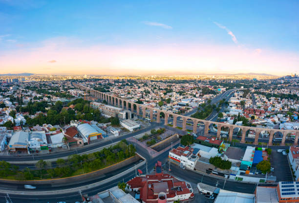 Aerial panoramic view over the famous Querétaro Aqueduct in the center of the city surrounded by buildings with a beautiful sunrise in the background Air tour over the beautiful city of Querétaro in a quiet sunrise queretaro city stock pictures, royalty-free photos & images