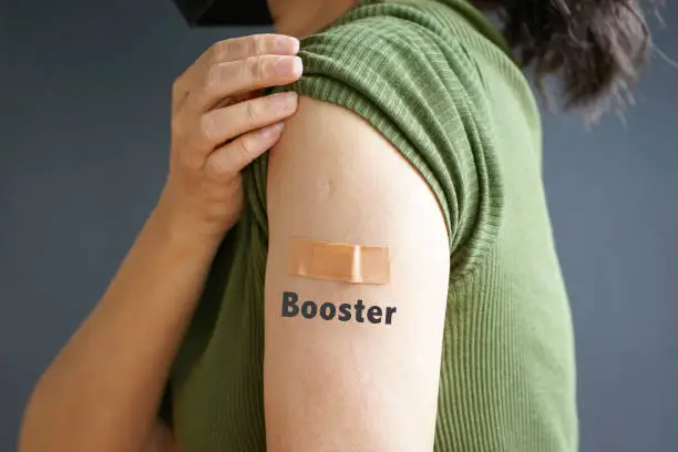 Close up view of woman arm with bandage and the word Booster - getting vaccinated immunity. Inoculation, vaccination, vaccinated patient concept.