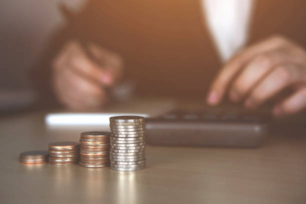 istock Coin stack and blurry of a young man pressing a calculator and taking notes. 1382698771