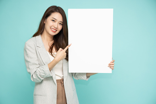 Asian business woman pointing and holding blank white billboard isolated on green background