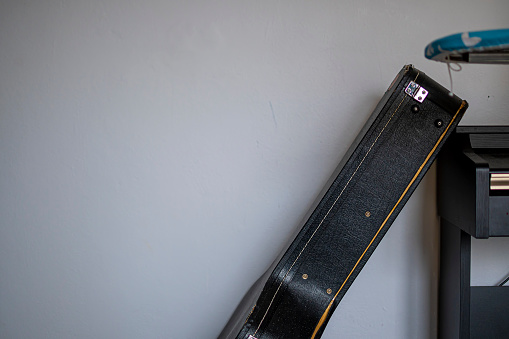 Black guitar case and a grey wall. Old leather encasement for a musical instrument. Indoor view in a room. Selective focus on the details, blurred background.