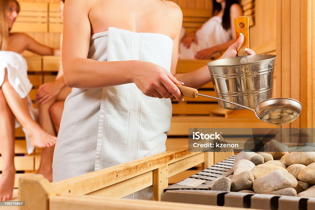 sauna wellness - four women in Spa Wellness - young happy women in sauna of a Spa, water and scent are splashed on hot stones for steam Heat - Temperature Stock Photo